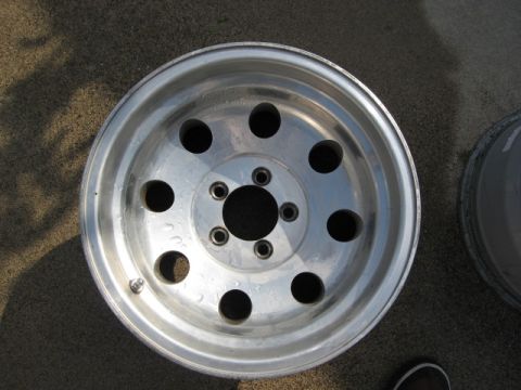 1986 Ford Bronco - A single aluminum wheel is shown lying on a textured surface, with another wheel partially visible to the right.