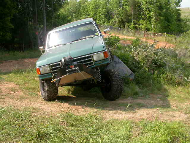 Lifted green Ford SUV with winch bumper flexing off-camber on a grassy trail