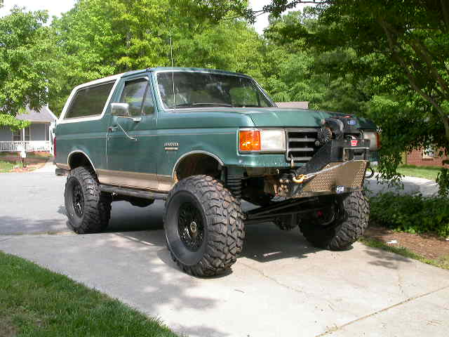 Green lifted Ford Bronco with white top and exposed front winch mount plate on a driveway