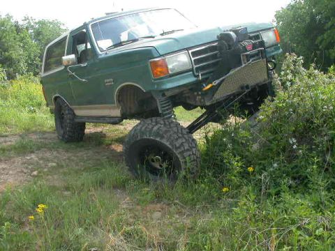 1990 Ford Bronco - Green Ford Bronco with white top and tan lower stripe flexing in a grassy field, front passenger tire lifted and the driver-side front droo…