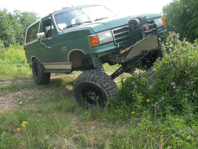 Green Ford Bronco flexing its front suspension in a grassy field with winch bumper