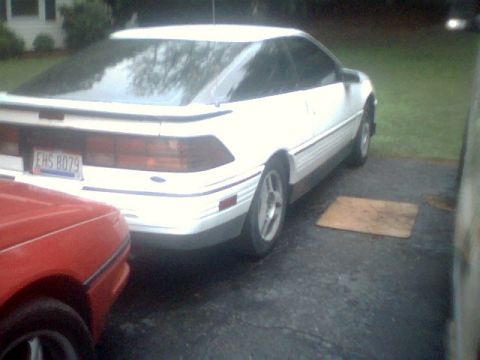 1989 Ford Probe - A white coupe with a spoiler is parked in a driveway next to a red car. The license plate is visible.