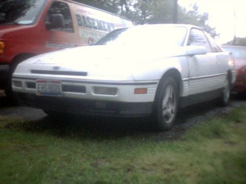 1989 Ford Probe - A white 1989 Ford Probe is seen from the front, parked on grass with a red van in the background.