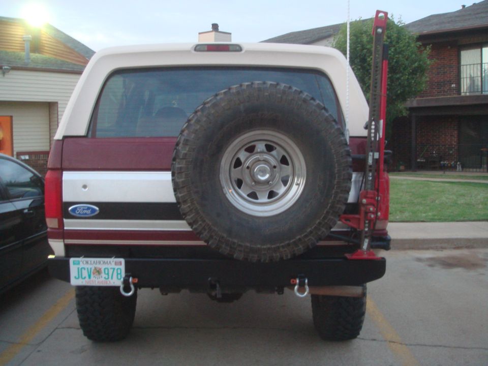 Rear of two-tone burgundy/cream Ford SUV with steel bumper, swing-out spare carrier and Hi-Lift jack