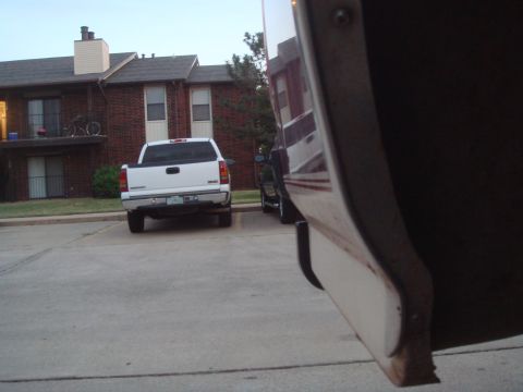1992 Ford Bronco - Low sightline down the side of a burgundy and cream SUV's rear quarter and black steel bumper corner in the right foreground, looking past…