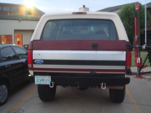 1992 Ford Bronco - The rear of a red and white Ford Bronco is visible, a custom bumper and a license plate reading "JCV 978".