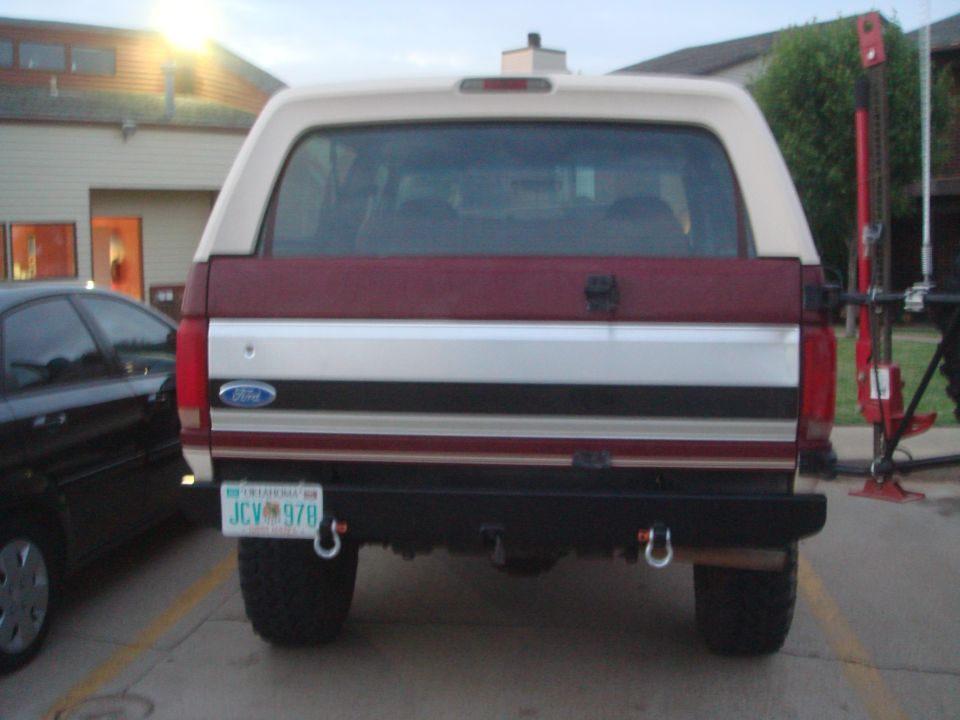 Red and white Ford Bronco rear view with "JCV 978" license plate and aftermarket bumper
