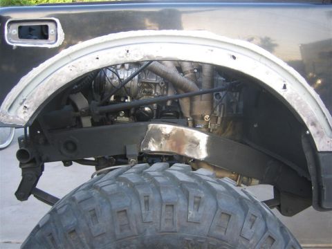 1987 Suzuki Samurai - Close-up of the fender well and suspension on a 1987 Suzuki Samurai, indicating bodywork in progress.