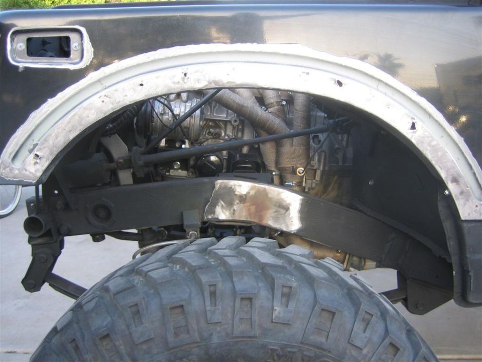 Cut and welded front fender opening with bare weld seam above a mud-terrain tire