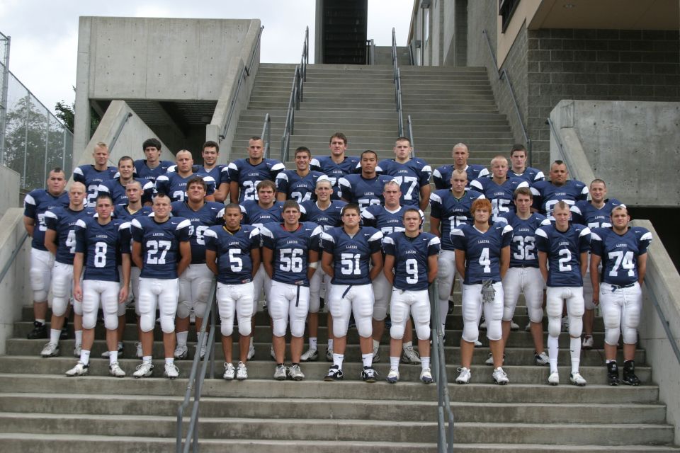 Football team posing on stadium stairs. Players wear navy blue uniforms with white numbers