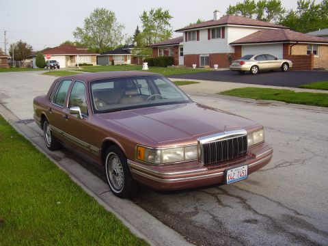 1996 Ford F-150 - A brown Lincoln Town Car is parked on the side of a residential street with houses in the background.