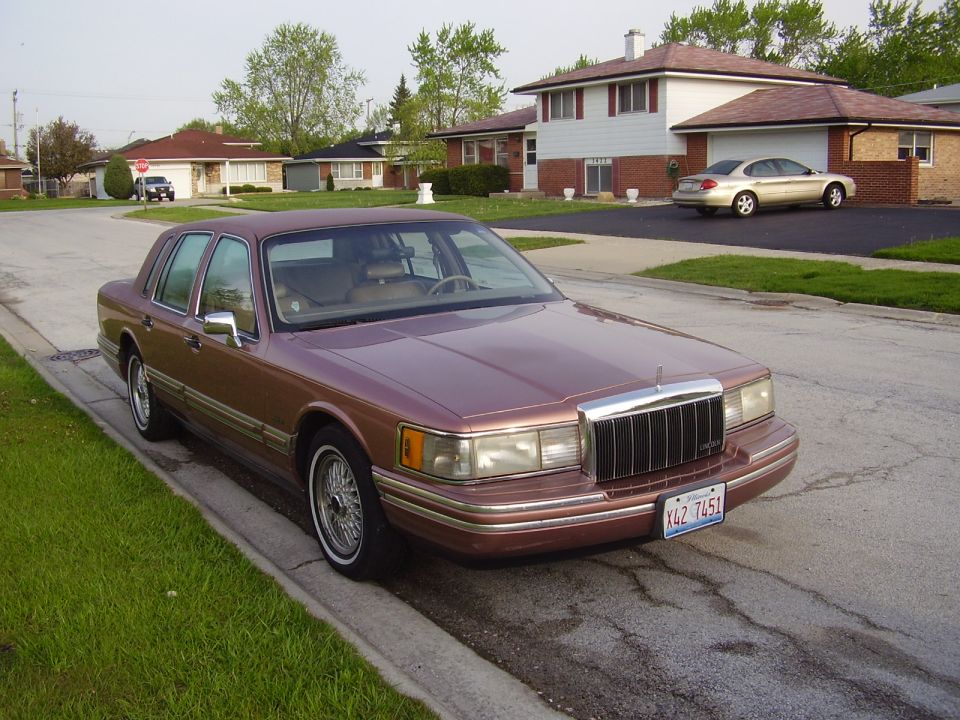 Brown Lincoln Town Car parked on street, suburban houses in background