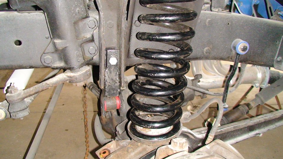 close-up of a vehicle's front suspension with a large coil spring and various metal linkages