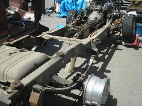 1986 Ford Bronco - The chassis and engine of a vehicle are shown disassembled, with the fuel tank and one wheel removed.
