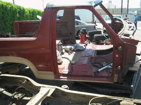 1986 Ford Bronco - Disassembled 1986 Ford Bronco body sits on a trailer, revealing its chassis and interior components.
