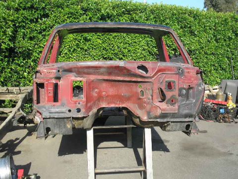 1986 Ford Bronco - The stripped body of a vehicle is shown on a stand, with a dense green hedge in the background.