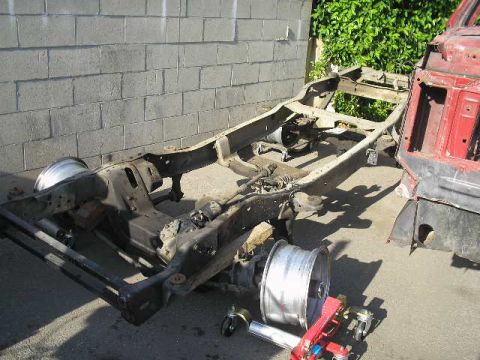 1986 Ford Bronco - The chassis and a portion of the body of a vehicle are disassembled and resting on the ground.