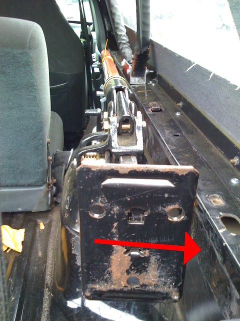 1993 Ford Bronco - A Hi-Lift jack is mounted inside a vehicle, next to a grey seat, with a red arrow pointing to the right.