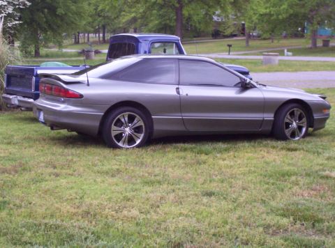 1995 Ford Probe - This 1995 Ford Probe is seen from the side, parked on grass next to a blue pickup truck.