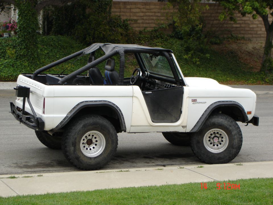 White early Ford Bronco, side view, top and doors off, on oversized tires with a lift