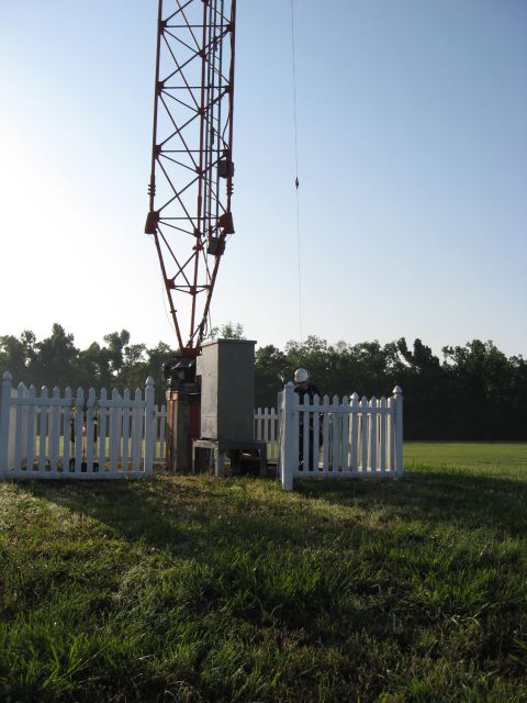2006 Ford F-150 - A person in a hard hat stands near the base of a cell tower, surrounded by a white picket fence and equipment.