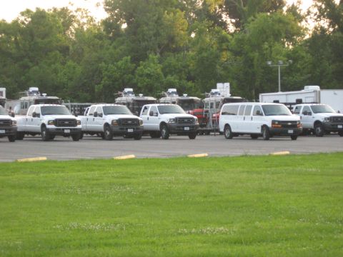 2006 Ford F-150 - A fleet of white pickup trucks and a van are parked in an outdoor lot with trees in the background.