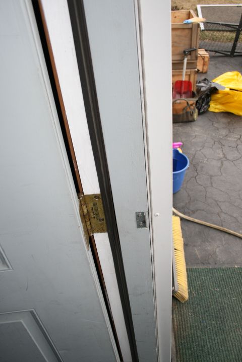 2003 Jeep TJ - Close-up of a door hinge with readable text, set against a white door frame and an outdoor scene.