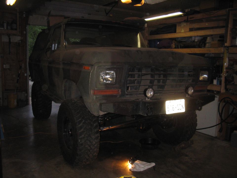 Camouflaged Ford Bronco with lifted suspension and off-road tires parked in a garage