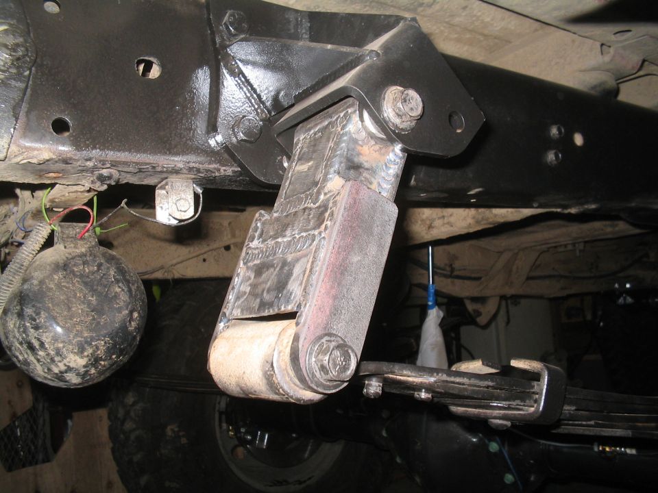 Close-up of a custom-welded suspension component attached to a vehicle frame, with a black spherical object and wiring visible
