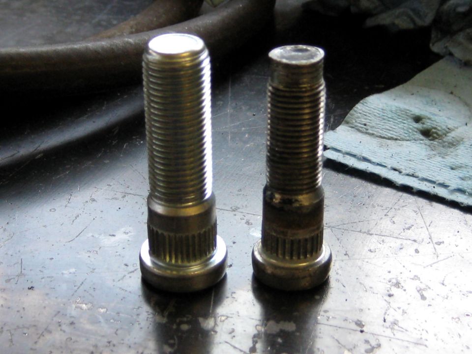 Two metal wheel studs on a workbench, one new and one worn