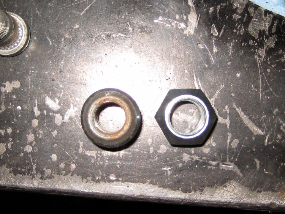 Two nuts on a metal surface: one is a rusty, round nut, the other is a new, black, hexagonal nut