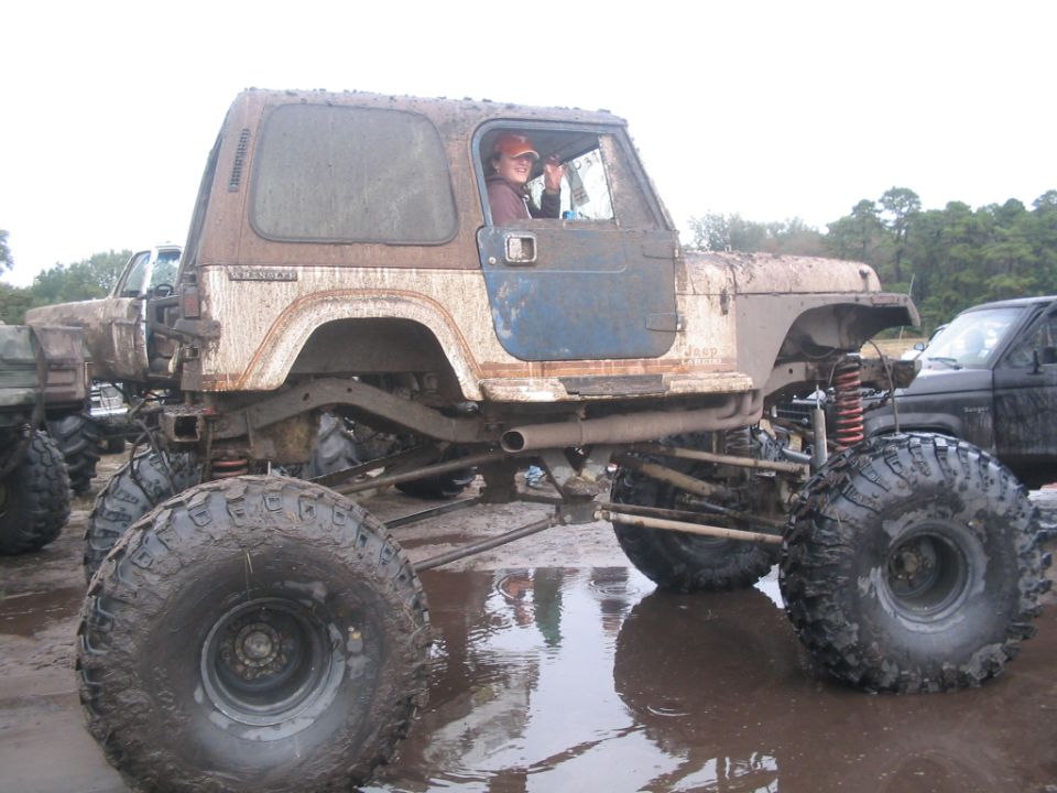 Mud-covered Jeep CJ-7 with lifted suspension and oversized tires, driver visible
