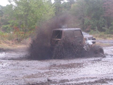 1990 Ford Bronco - Vehicle powers through a muddy off-road course, creating a significant splash.