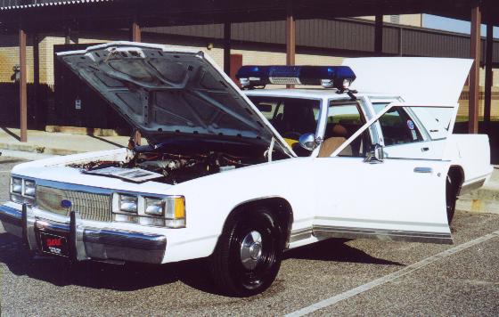 White Crown Victoria police car on display with hood, doors and trunk open, roof light bar visible