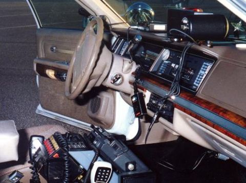 1991 Ford Crown Victoria - The interior of a 1991 Ford Crown Victoria police car, equipped with various radio communication devices and a light bar on the dashboard.