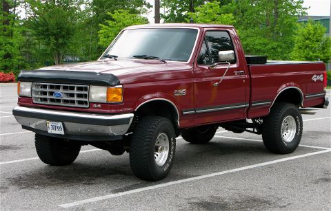 1991 Ford F-150 - This maroon Ford F-150 pickup truck is shown from a 3/4 front angle, parked in a lot with trees in the background.