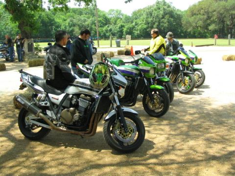 1981 Kawasaki Bayou - Several motorcycles are parked outdoors on a sunny day, with people standing around them.