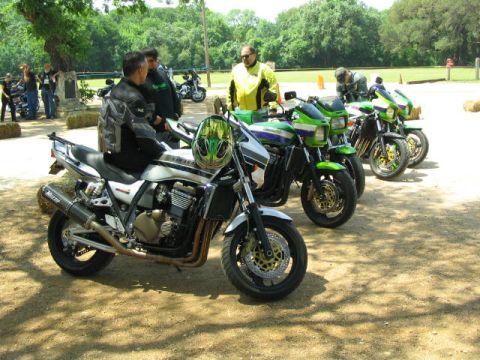 1981 Kawasaki Bayou - A group of motorcycles are parked on a dirt lot, with several people gathered around them.