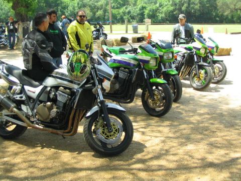 1981 Kawasaki Bayou - A group of people stand near several parked motorcycles on a sunny day.