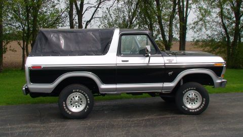 1979 Ford Bronco - This two-tone Ford Bronco is parked on a paved surface with trees in the background.