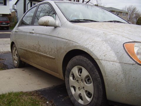 1996 Ford F-150 - A silver sedan is parked on a concrete driveway, heavily covered in mud and dirt. The front passenger side of the vehicle is visible, showi…