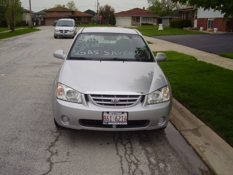 1996 Ford F-150 - A silver Kia Spectra is parked on a residential street with a "For Sale" sign written on the windshield. The car has a license plate from I…
