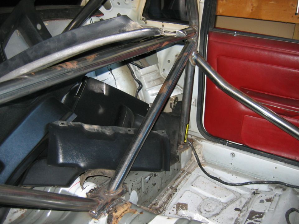 Interior of a car with a roll cage, red door panel, and stripped floor.