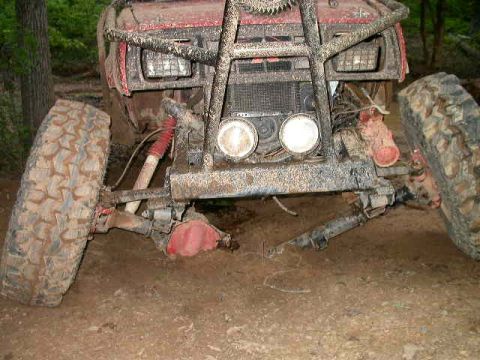 1990 Ford Bronco - The front end of a heavily mud-covered off-road vehicle, likely a 1990 Ford Bronco, is shown angled towards the viewer. The vehicle has lar…