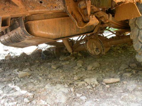 1990 Ford Bronco - Underside view of a heavily mud-covered vehicle, showing the fuel tank, leaf springs, and rear differential. The vehicle appears to be an o…