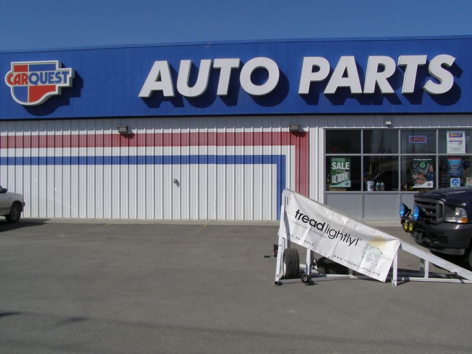 Dark Ford truck parked in front of Carquest Auto Parts store with a tread lightly banner.