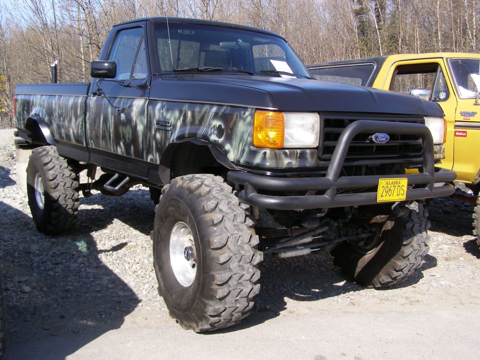 Lifted black Ford pickup truck with camouflage paint, large tires, and bull bar.