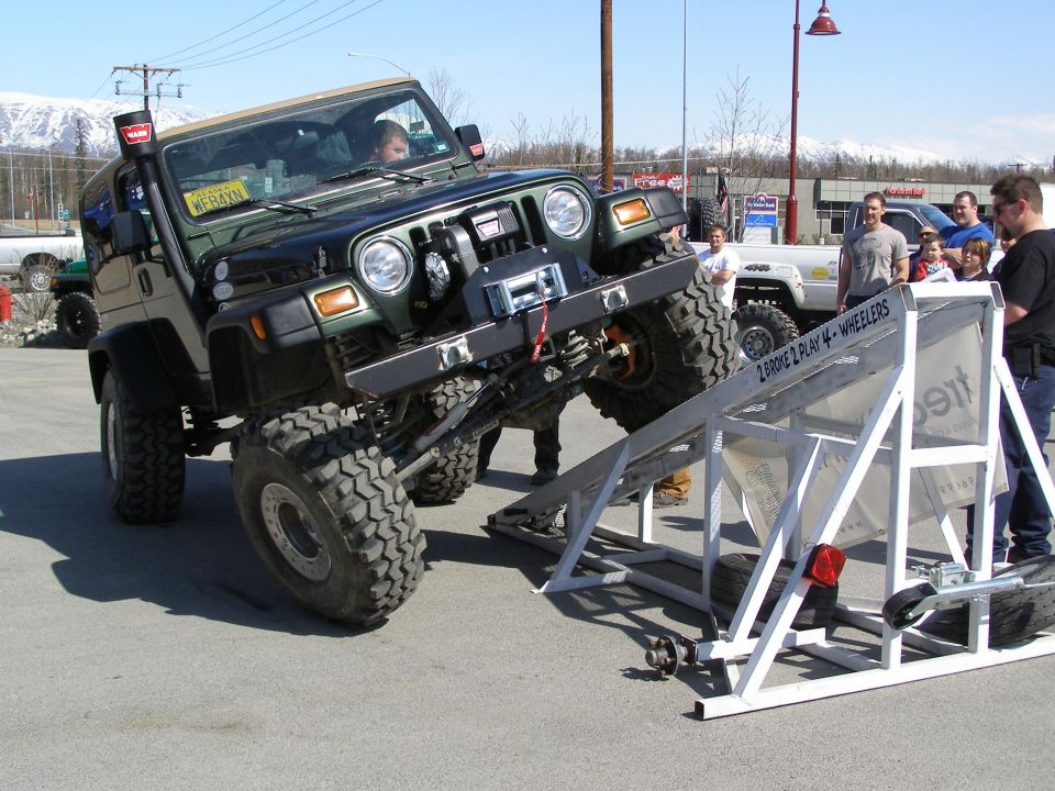 Lifted green Jeep Wrangler on a metal ramp with people watching.