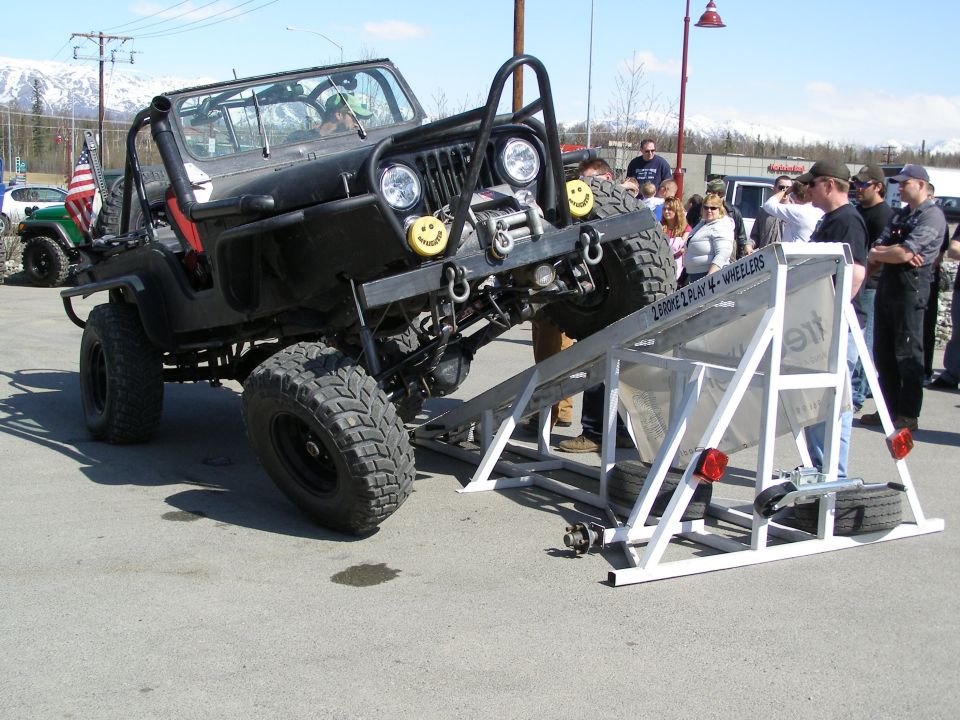 Modified black Jeep Wrangler on a ramp with people watching.