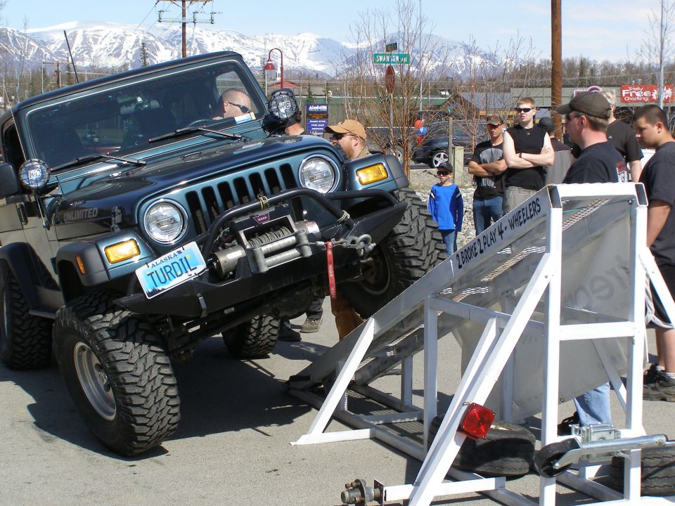 Teal Jeep Wrangler on a metal ramp with off-road tires. Alaska license plate reads TURDIL.